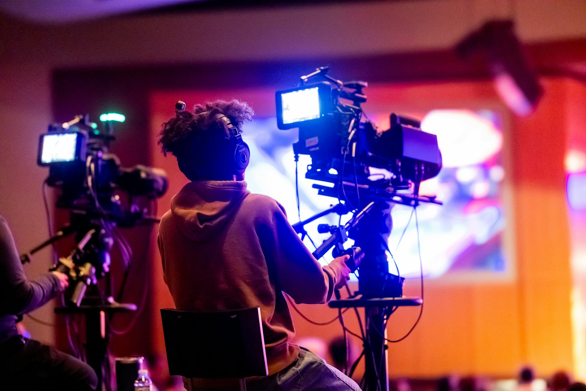 Back view of a videographer operating a camera at a live event, focusing on a vibrant indoor setup.