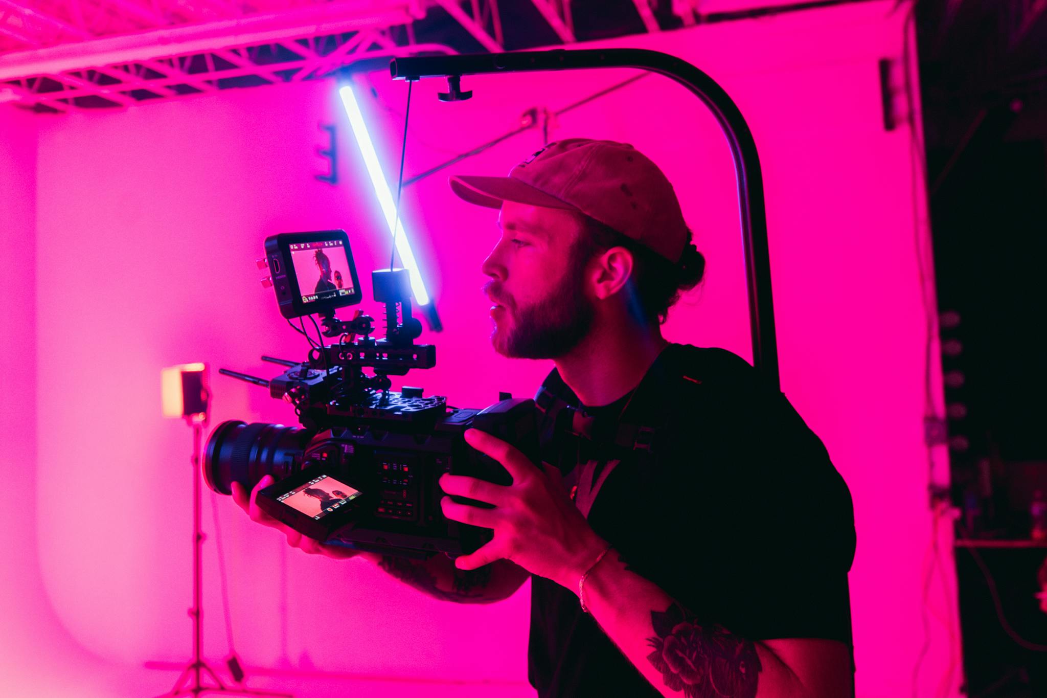 Bearded videographer in a neon-lit studio filming with professional camera setup.